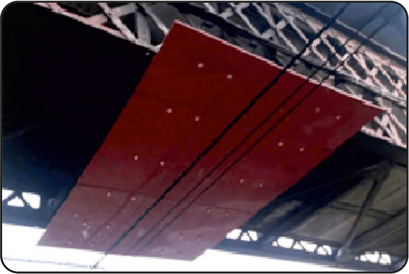 Red barrier board panels bolted flat to the underside of a steel roof truss, with two bare conductors crossing beneath them.