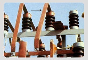 Copper flat busbars carried on brown post insulators in an outdoor switchyard structure, with an arrow marking one vertical bar