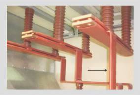 Red-sleeved rectangular busbar risers inside a panel, rising to post insulators mounted on a horizontal bar above